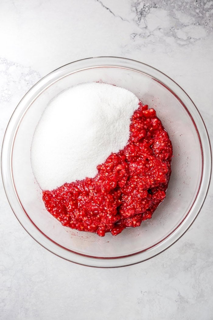 Overhead view of sugar and mashed raspberries in bowl