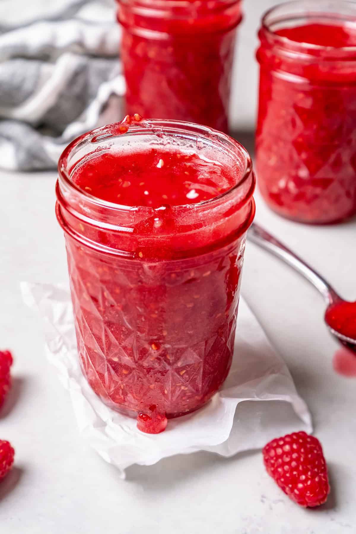 Open jar of raspberry freezer jam, with additional jars in background