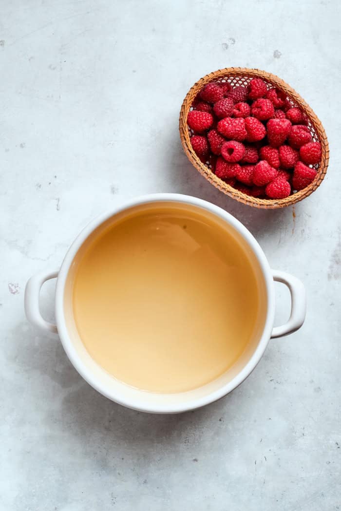 Made with just 3 simple ingredients, this homemade raspberry vinegar recipe is incredibly easy and fantastic for dressings, drinks and more! Vinegar and sugar mixture in pot set next to basket of raspberries.