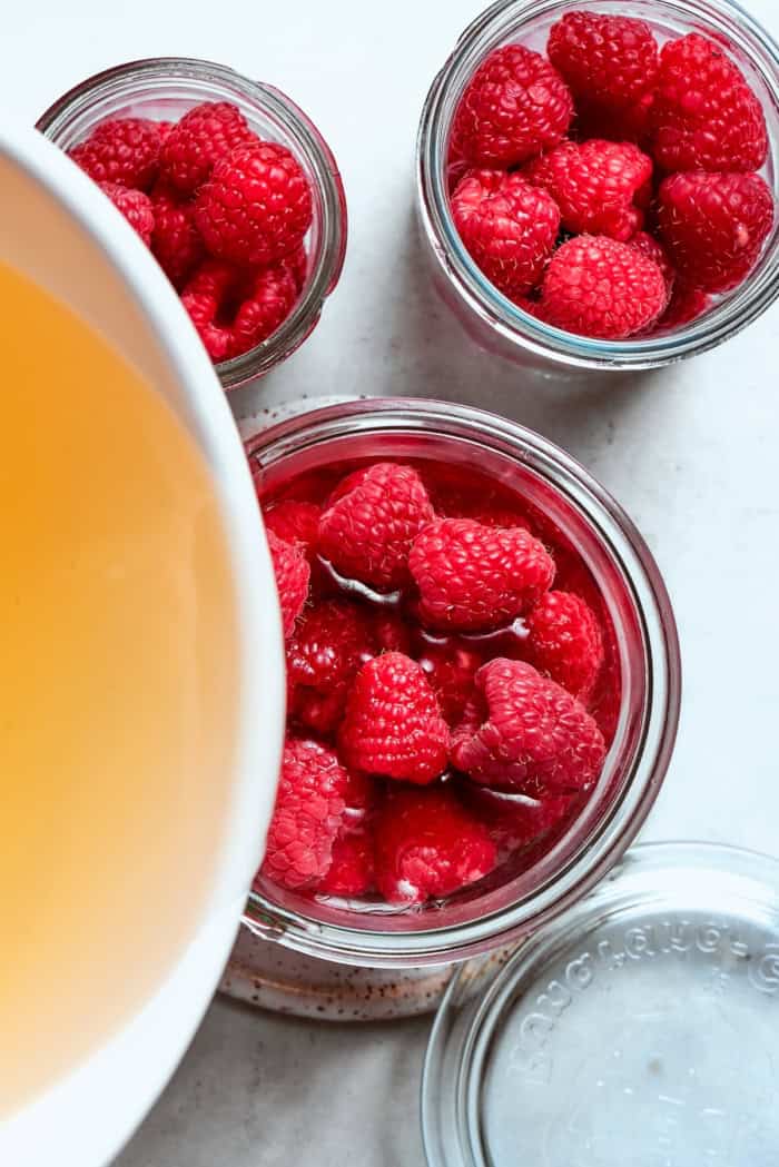 Made with just 3 simple ingredients, this homemade raspberry vinegar recipe is incredibly easy and fantastic for dressings, drinks and more! Pouring vinegar mixture into jars of raspberries.