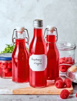 3 bottles of homemade raspberry vinegar on wooden board.