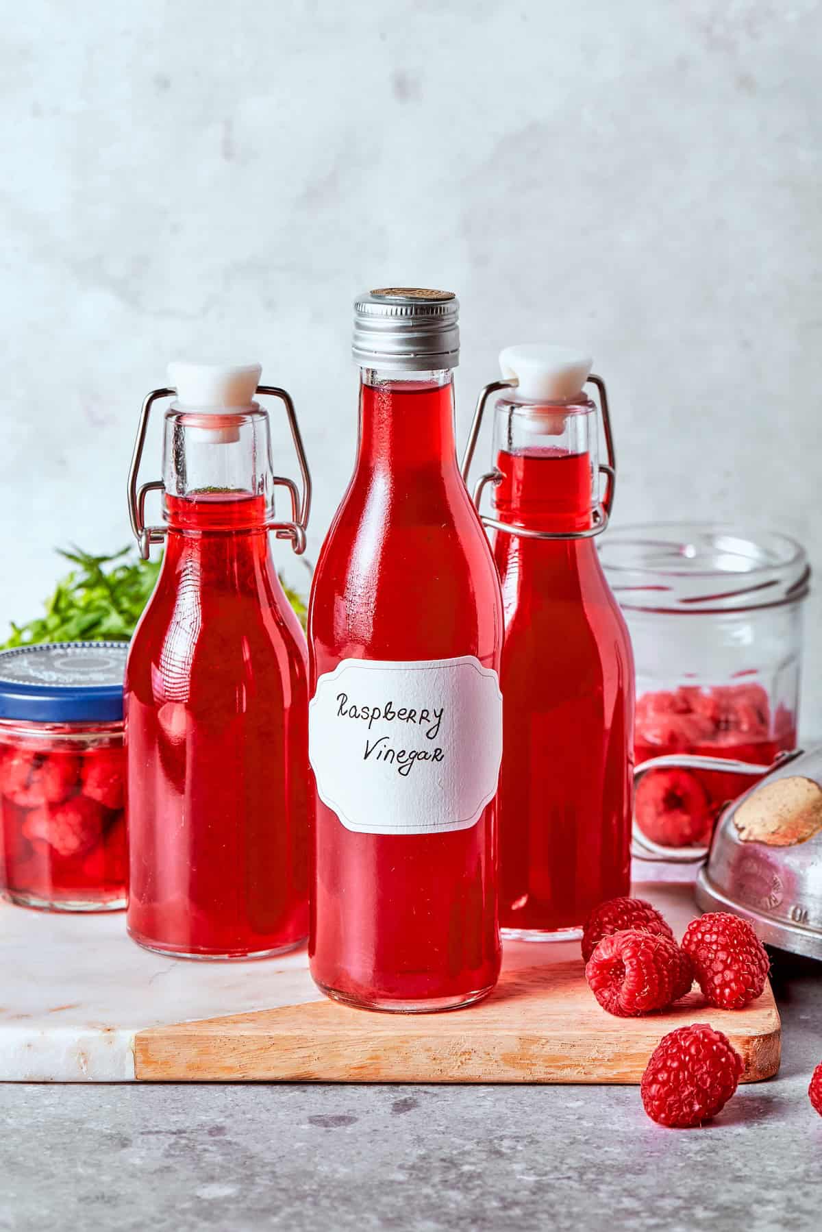 Made with just 3 simple ingredients, this homemade raspberry vinegar recipe is incredibly easy and fantastic for dressings, drinks and more! 3 bottles of homemade raspberry vinegar on wooden board.
