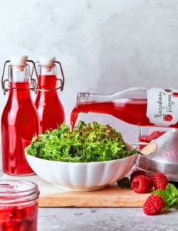 Pouring raspberry vinegar into bowl of greens.