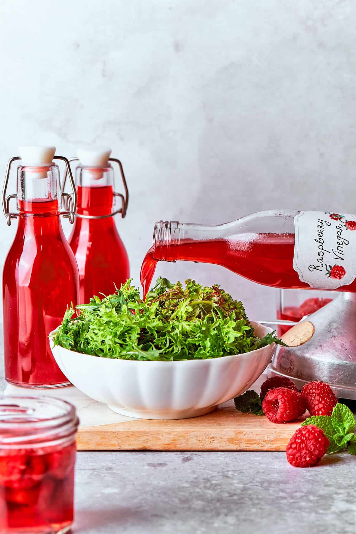 Made with just 3 simple ingredients, this homemade raspberry vinegar recipe is incredibly easy and fantastic for dressings, drinks and more! Pouring raspberry vinegar into bowl of greens.