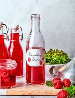 Bottle of raspberry vinegar with bowl of greens in background.