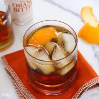 A Glass of Old Fashioned Bacon Bourbon on the Rocks Next to an Orange Peel