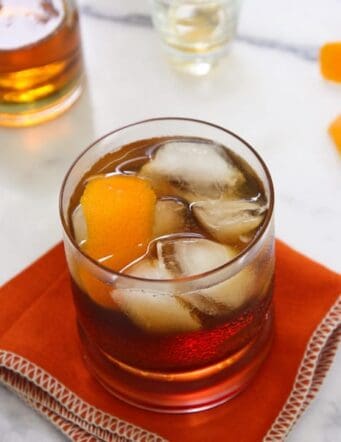 A rocks glass of Bacon Bourbon Old Fashioned with ice and orange peel