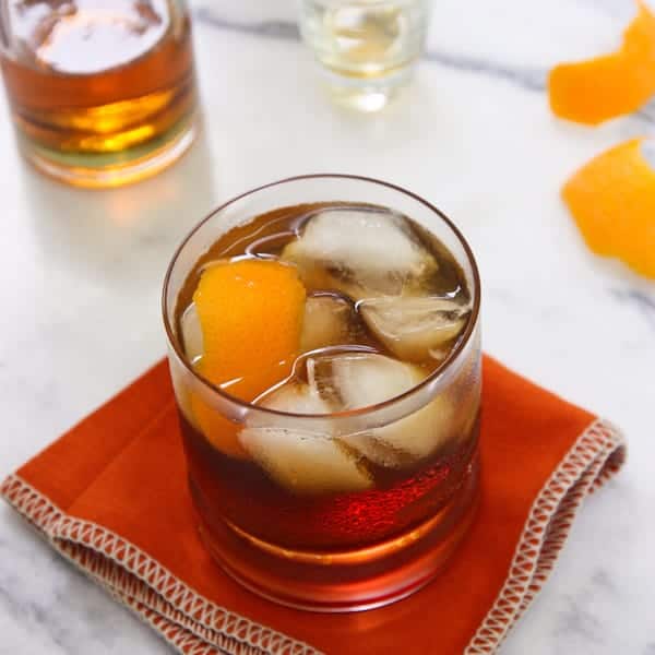 A rocks glass of Bacon Bourbon Old Fashioned with ice and orange peel
