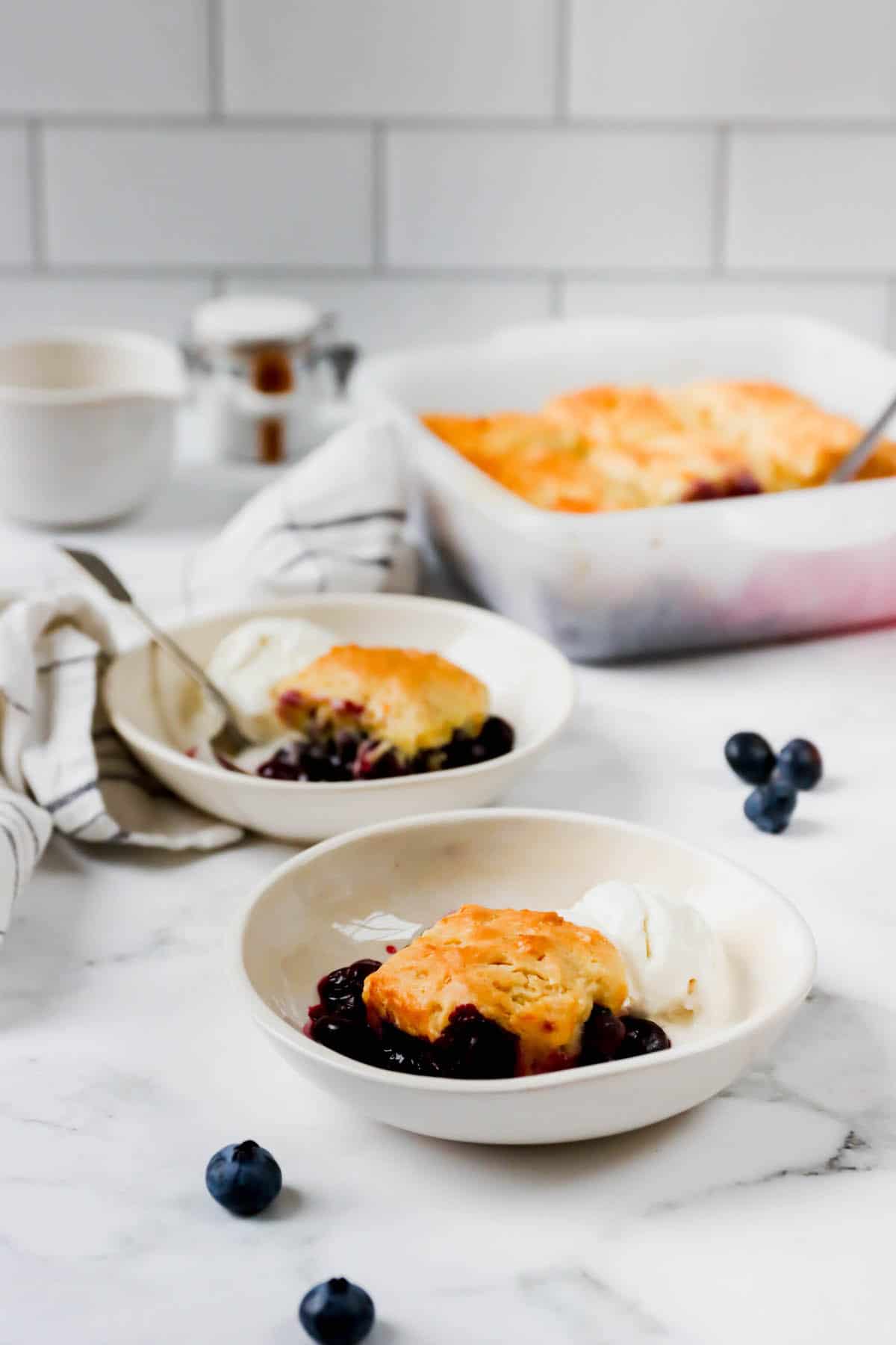 Two plates with blueberry cobbler and the baking dish in back