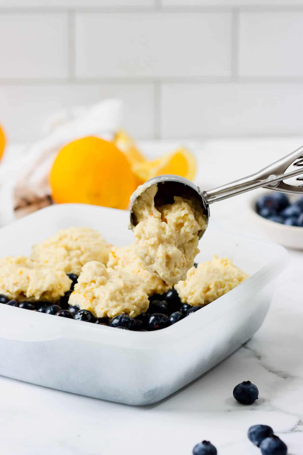 Orange biscuit dough being scooped into a baking dish of blueberry cobbler