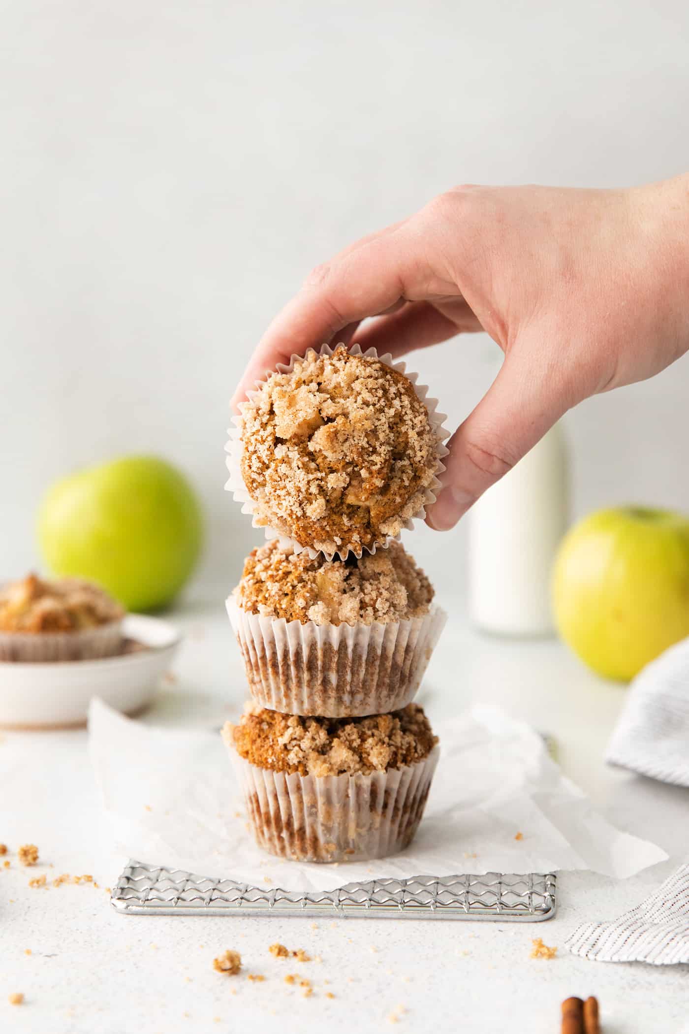 Three stacked apple muffins and a hand reaching for the top one