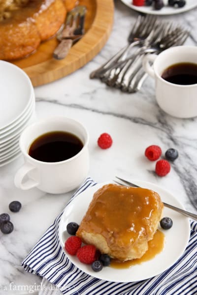 a caramel roll on a white plate with fresh berries and a cup of coffee