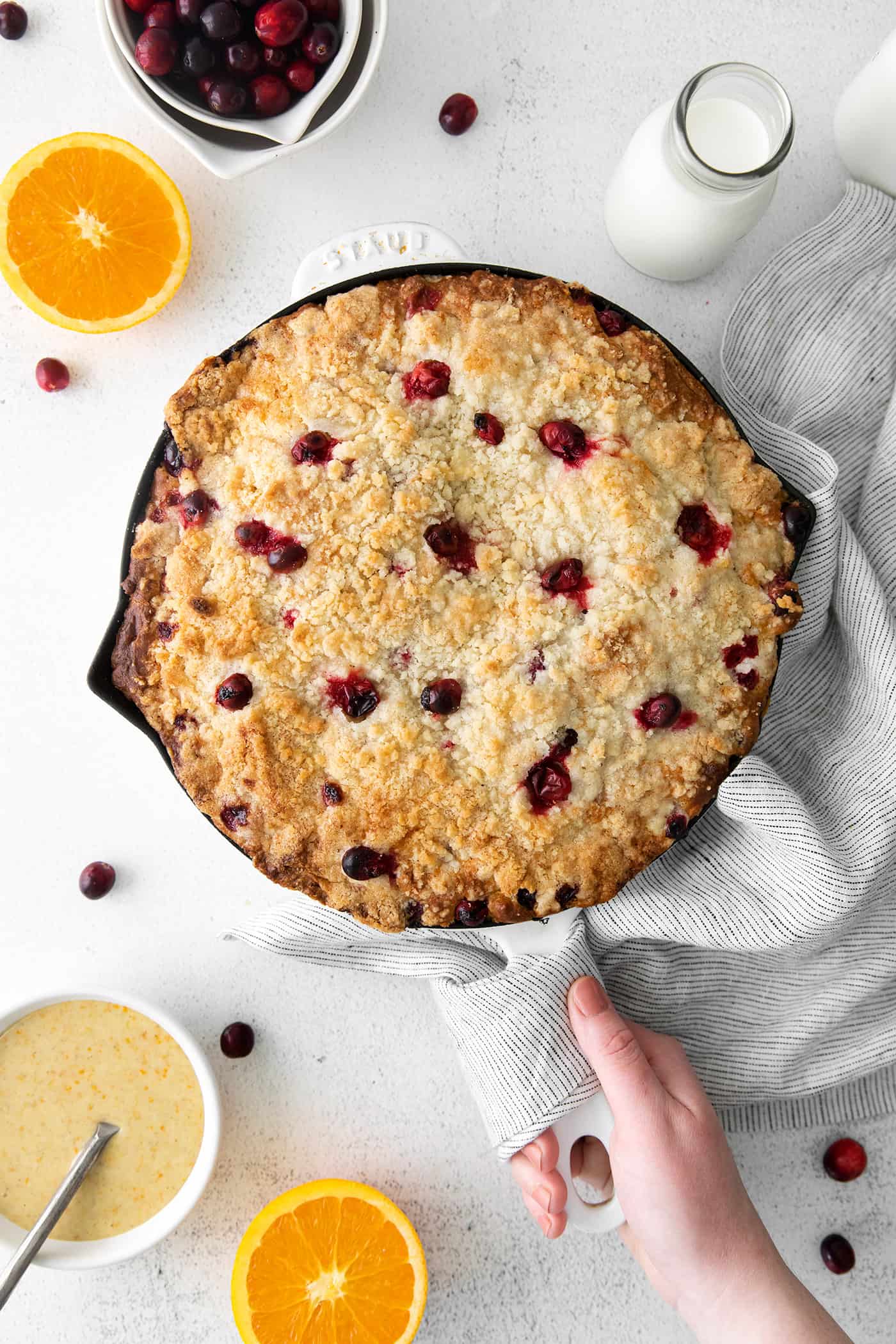 A hand holding a skillet of cranberry orange cake