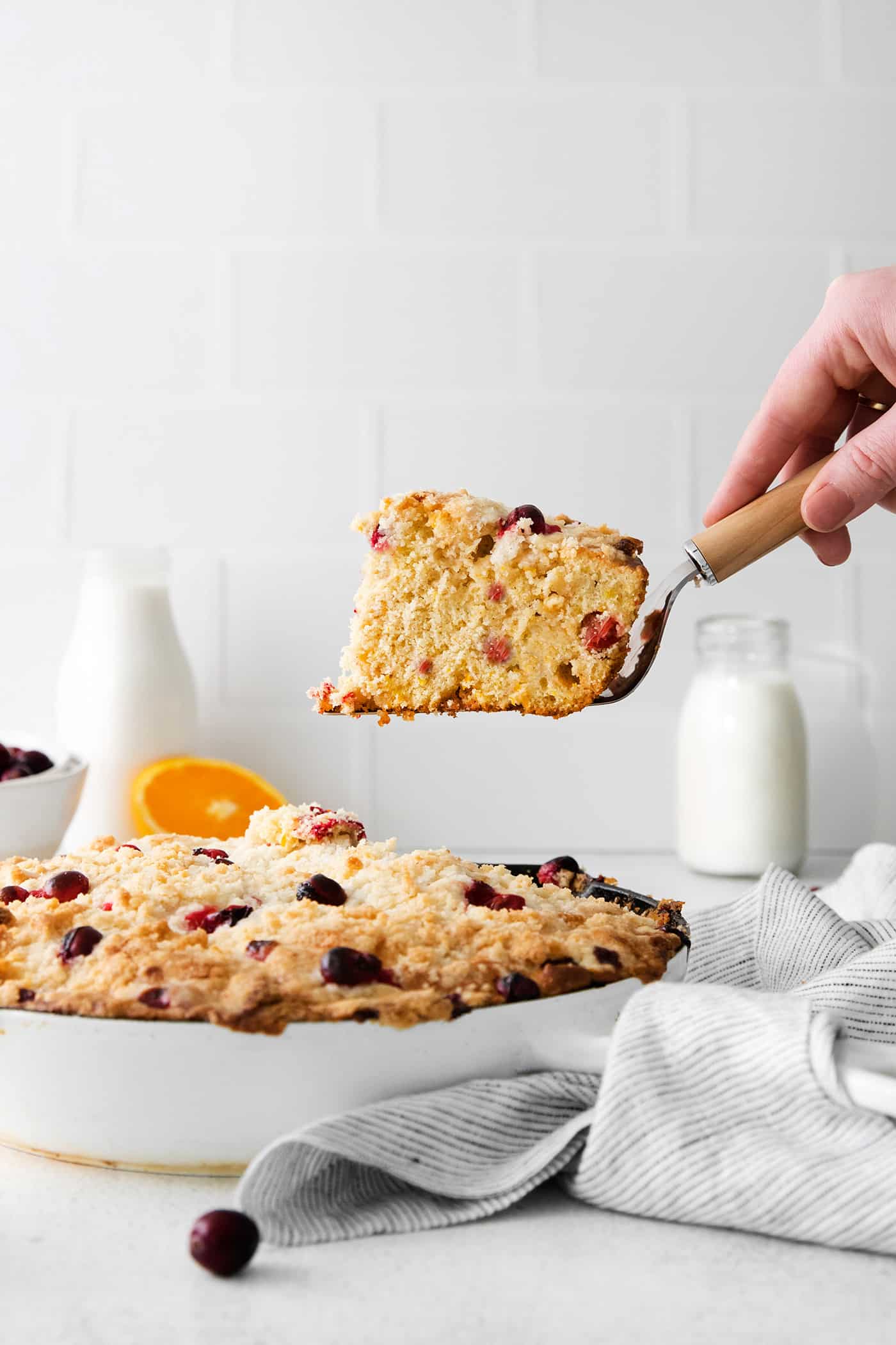 A hand serving a slice of cranberry orange skillet cake