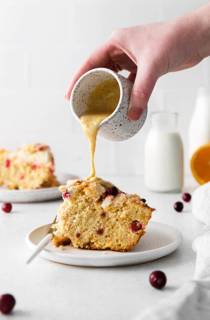 A hand pouring orange glaze over a slice of cranberry orange skillet cake