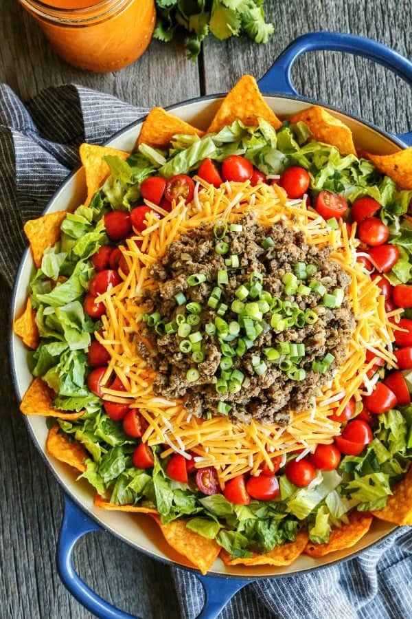 Dorito taco salad layered in a large blue bowl, with nacho cheese Doritos, lettuce, tomatoes, cheese, and taco meat