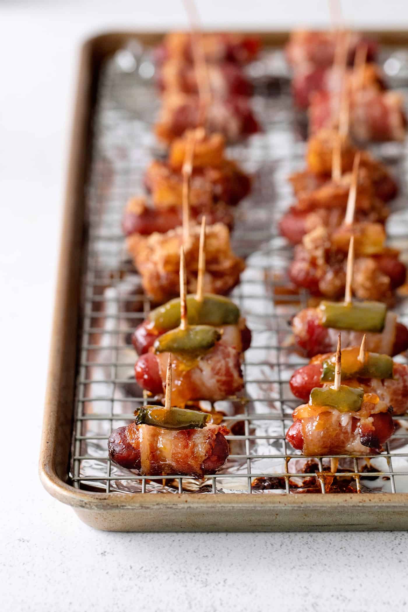 Angled view of bacon wrapped weiners on a baking sheet