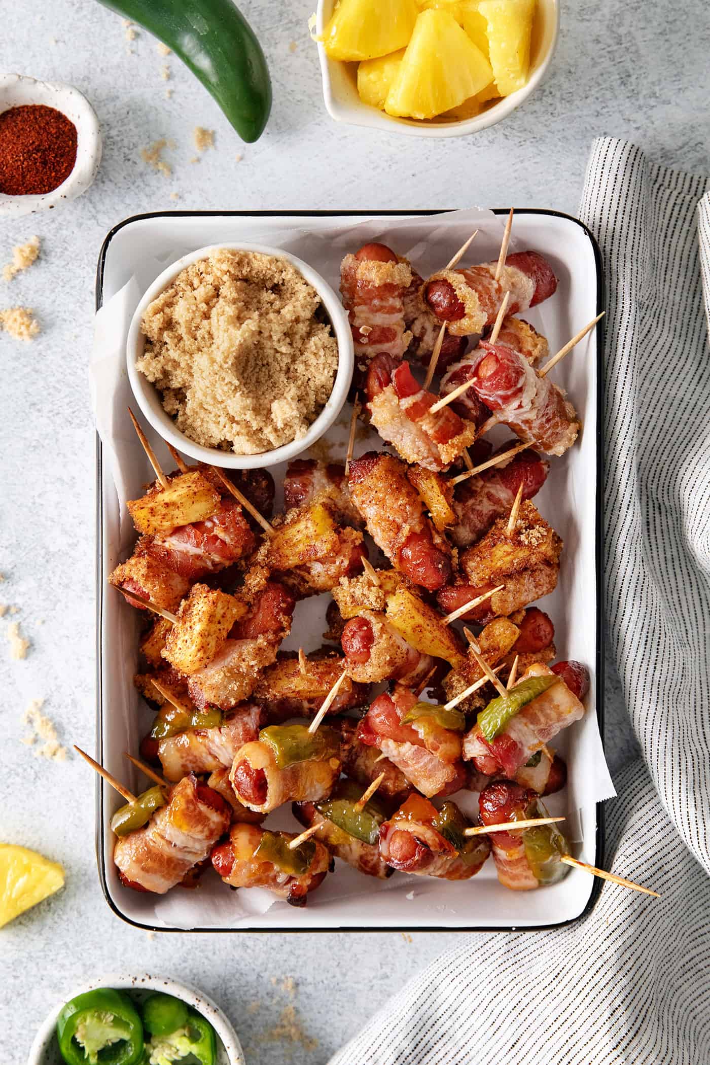 Overhead view of bacon wrapped little smokies on a serving platter with a bowl of brown sugar