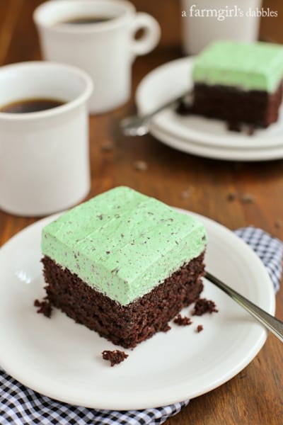 a slice of Chocolate Cake with Mint Buttercream on a white plate with a mug of coffee