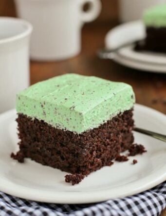 A square of chocolate cake with mint buttercream frosting on a white plate