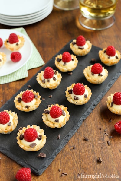 Phyllo Cups with Coconut Cream, Raspberries, and Dark Chocolate on a black board with glasses of white wine