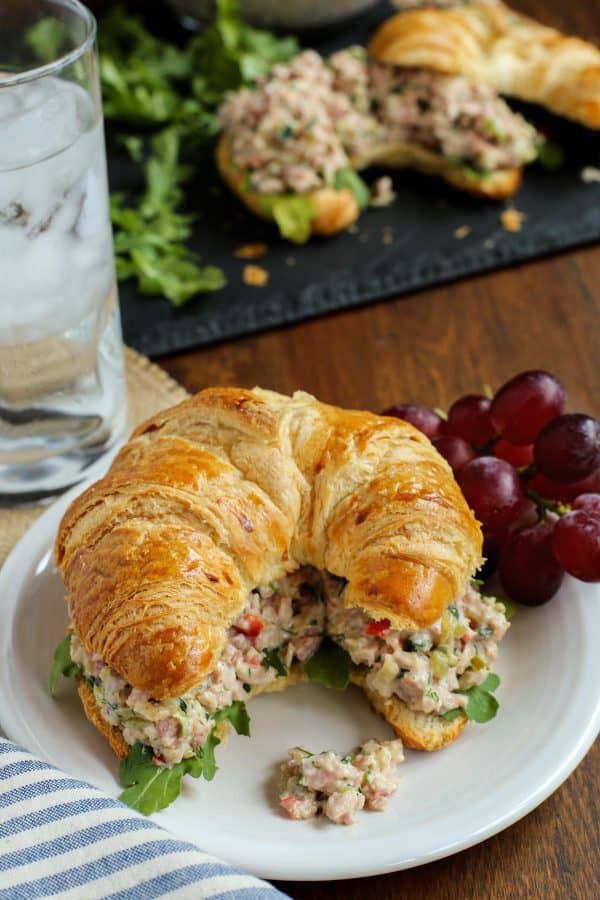 herby ham salad on a croissant with grapes and a glass of water