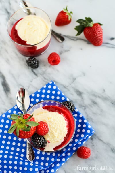 two glass ramekins of Crème Fraîche Ice Cream with Triple Berry Sauce drizzled on top