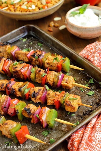 Grilled Charmoula Pork Kebabs on a baking pan with a bowl of Yogurt Mint Sauce