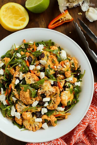 A white bowl filled with Cauliflower Salad topped with feta and raisins