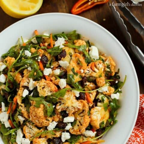 Cauliflower Salad with raisins, greens, feta and carrots in a white bowl