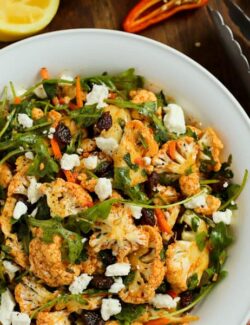 Cauliflower Salad with raisins, greens, feta and carrots in a white bowl