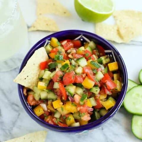 Pico de Gallo with diced cucumber, tomato, and peppers in a blue bowl with a tortilla chip