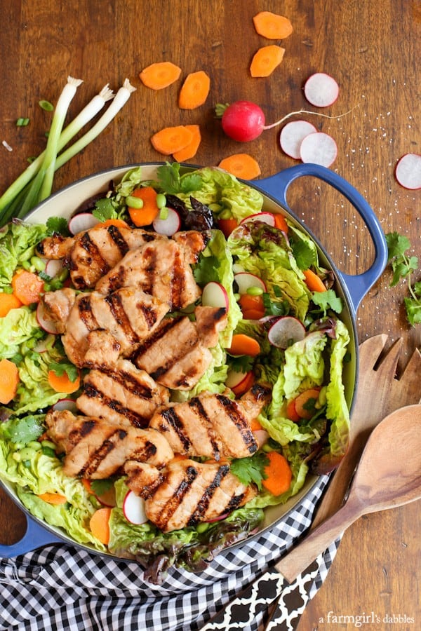 Asian Pork Tenderloin Salad in a blue bowl with wooden serving spoons