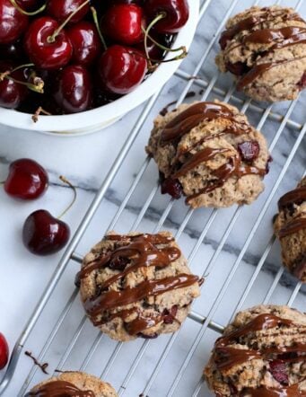 Round scones with cherries and dark chocolate drizzle on a cooling rack