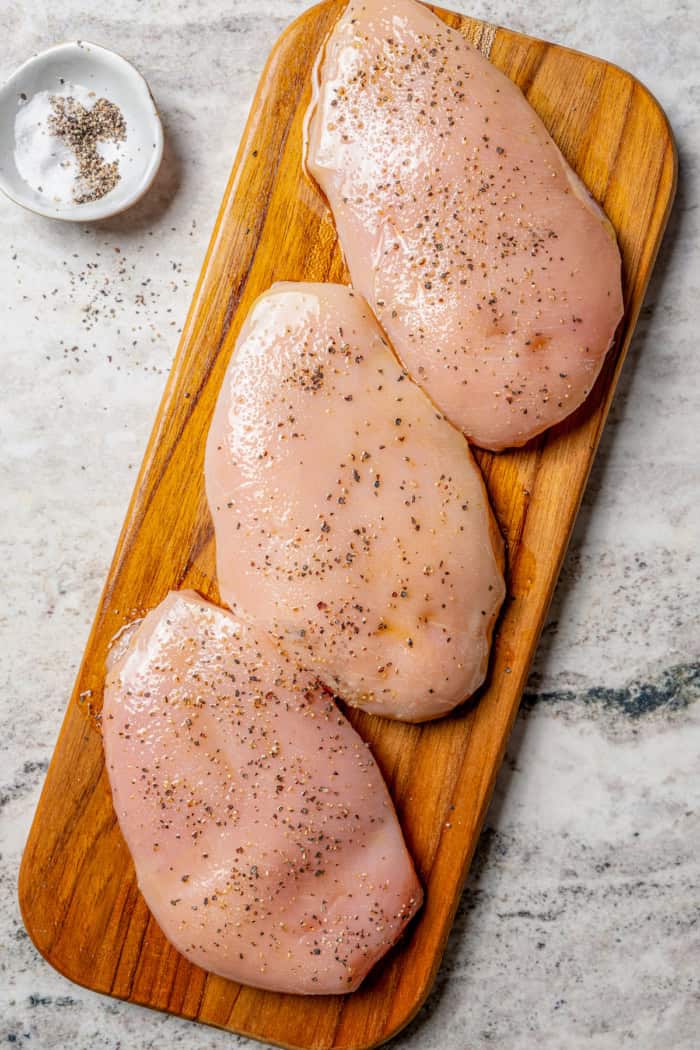 Seasoned chicken breasts on wooden board