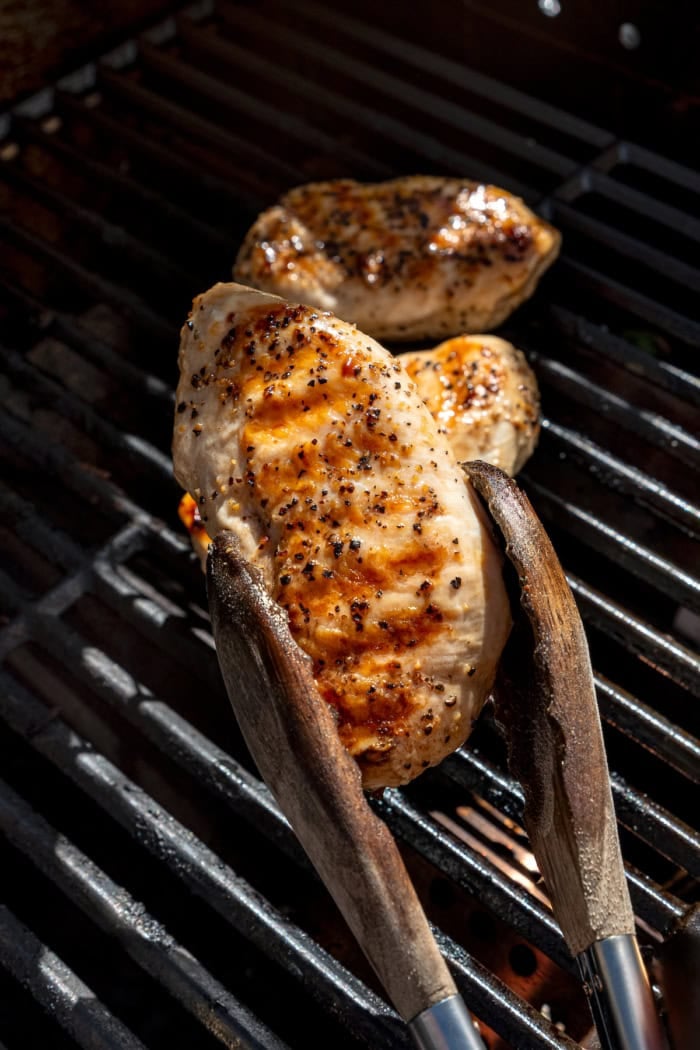 Tongs picking up grilled chicken breast