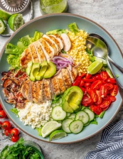 Overhead view of grilled chicken salad in bowl with two spoons