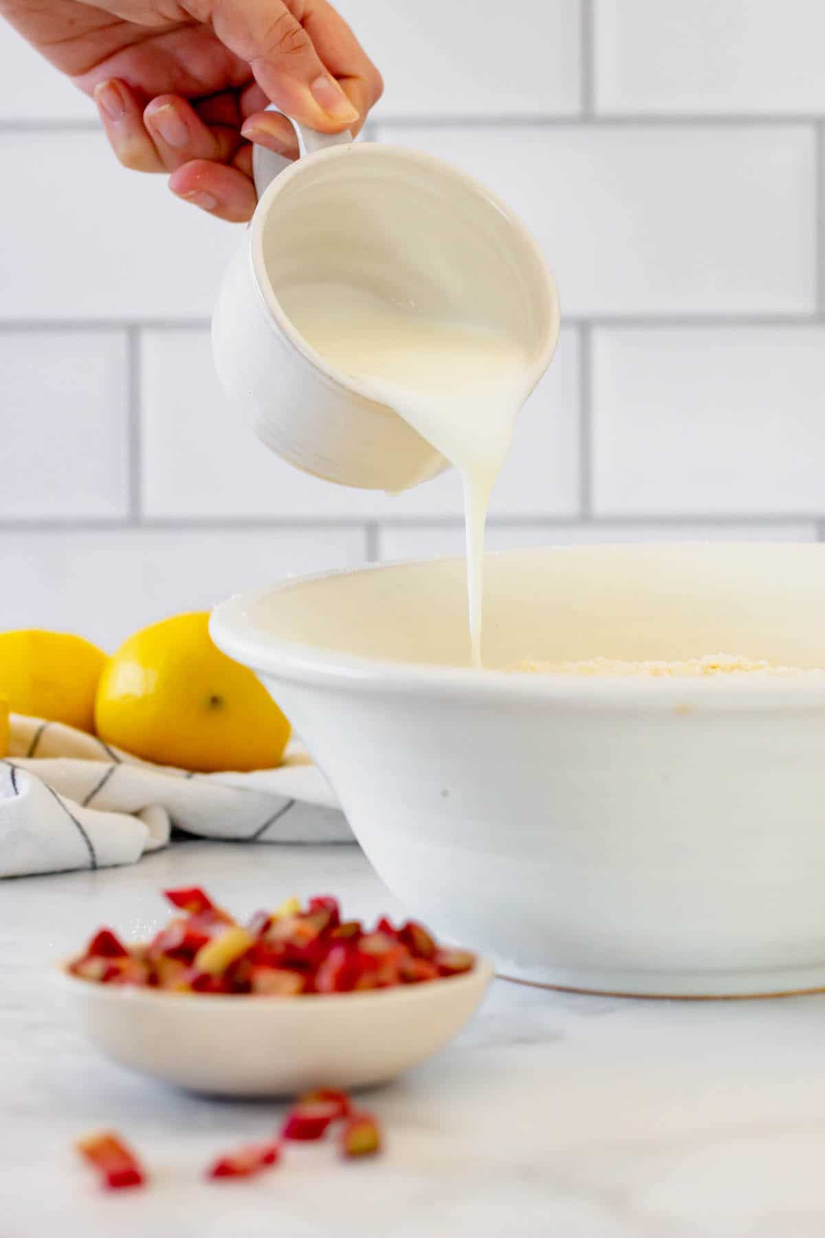 Milk being poured into a white bowl, with a dish of chopped rhubarb in front of it