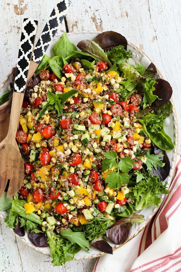 Quinoa, lettuce, and vegetables on a white serving plate with wooden serving spoons