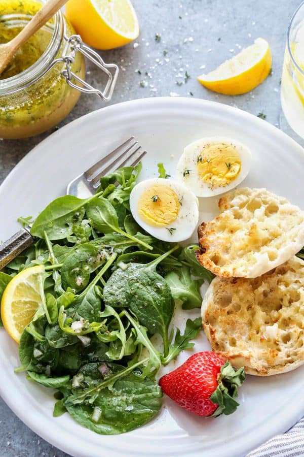 a plate with salad, english muffins, strawberries, and a hardboiled egg
