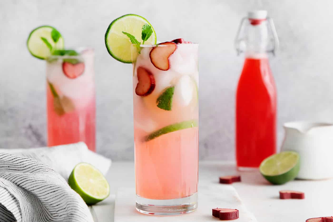 Two rhubarb mojitos and a bottle of rhubarb syrup in the background