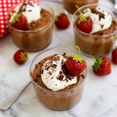 Chocolate mousse in glass cups topped with whipped cream, shredded chocolate, and a fresh strawberry