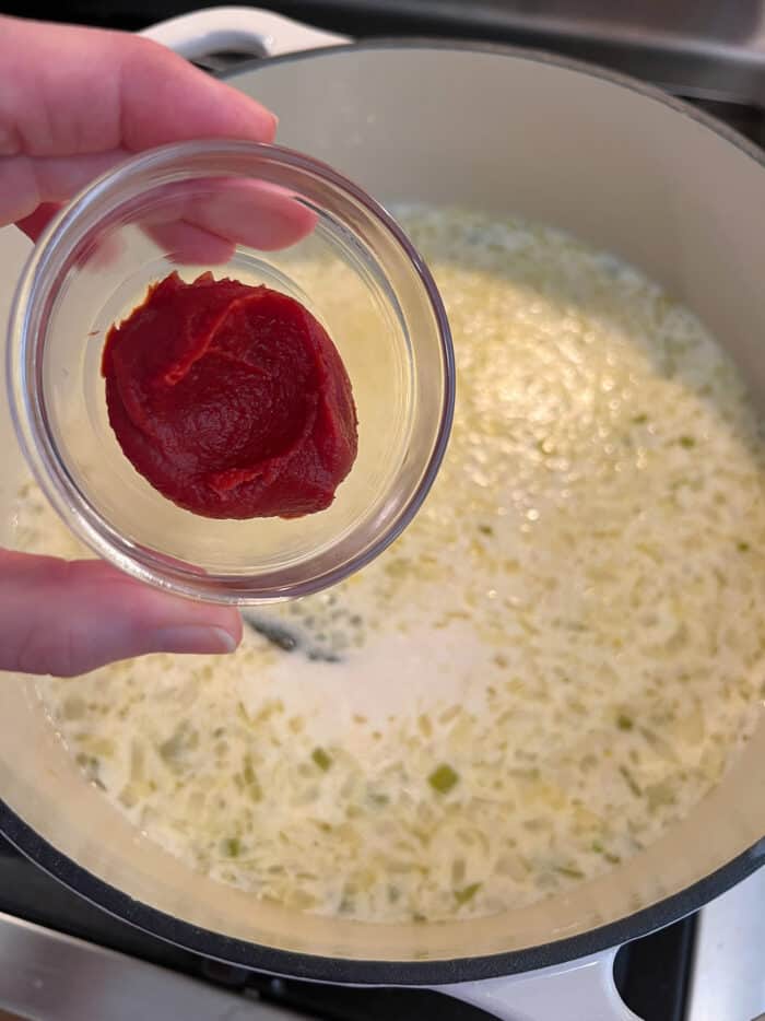 Tomato paste being held over a soup pan of broth