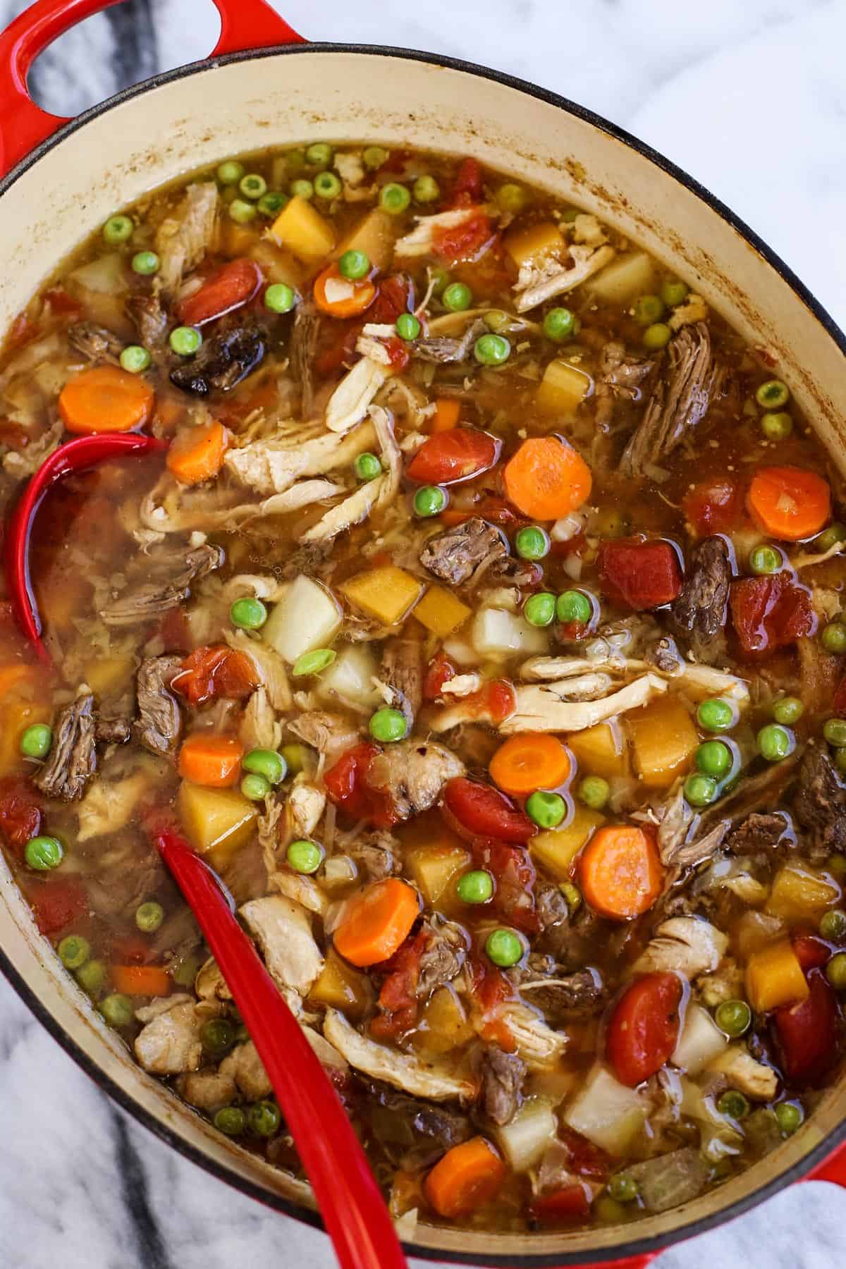 a large red pot of booyah soup, full of vegetables and meats