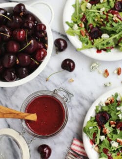 A bowl of cherries, two plates of salad and a glass jar of cherry-chipotle balsamic vinaigrette