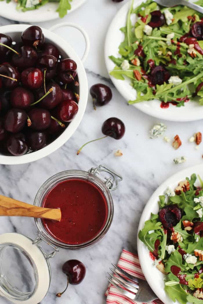 A bowl of cherries, two plates of salad and a glass jar of cherry-chipotle balsamic vinaigrette