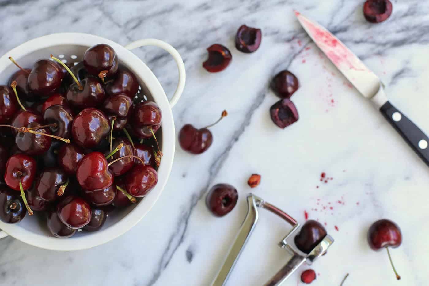 A bowl of cherries next to a cutting board where some cherries are being pitted and cut in half