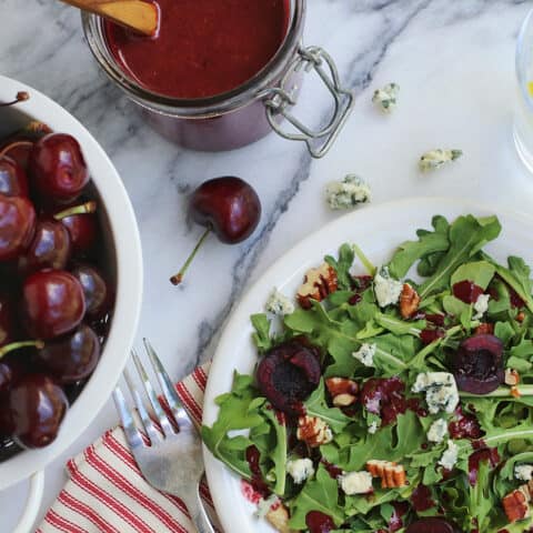 A bowl of cherries next to a salad topped with cherry-chipotle balsamic vinaigrette