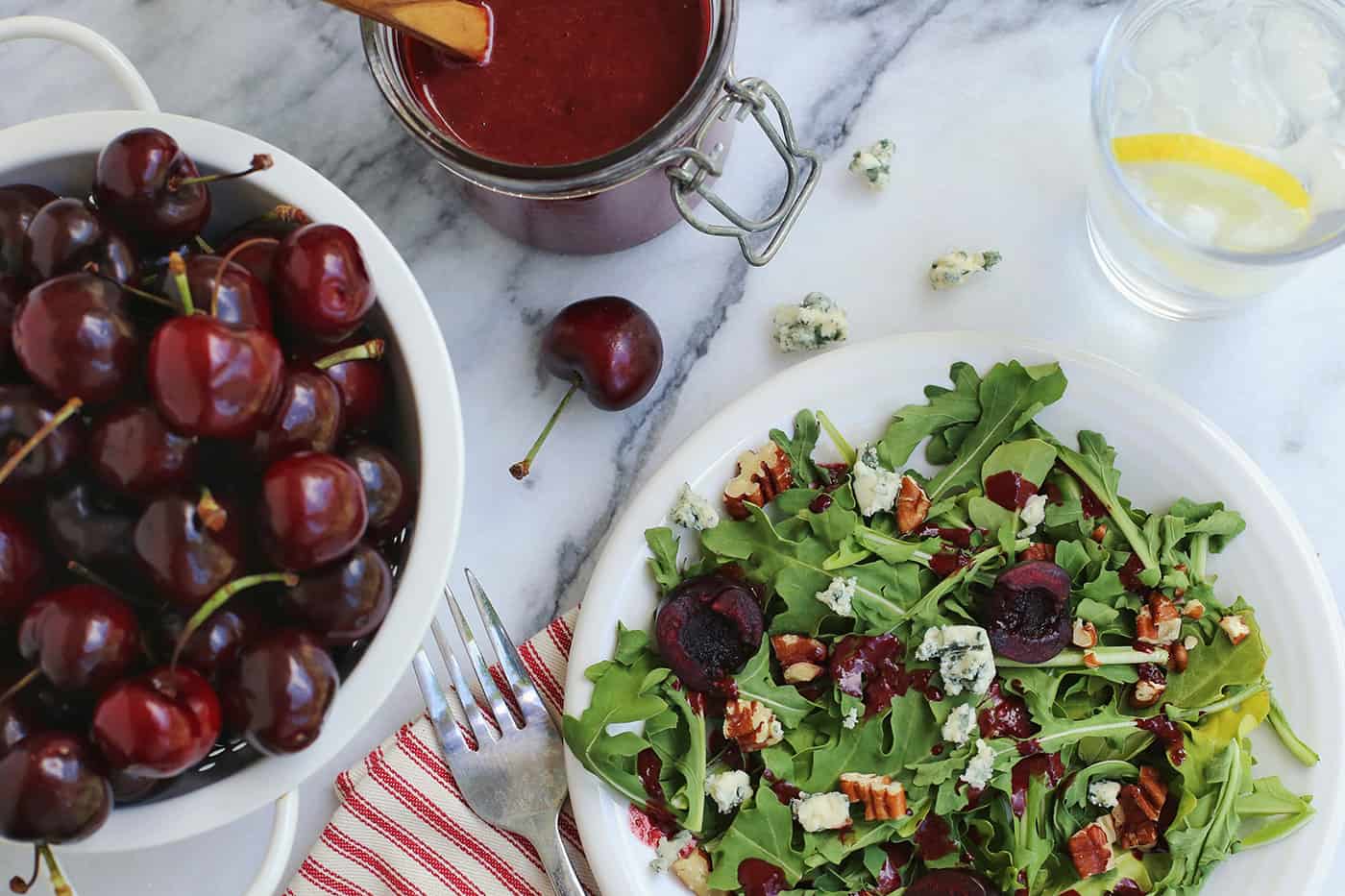 A bowl of cherries next to a salad topped with cherry-chipotle balsamic vinaigrette