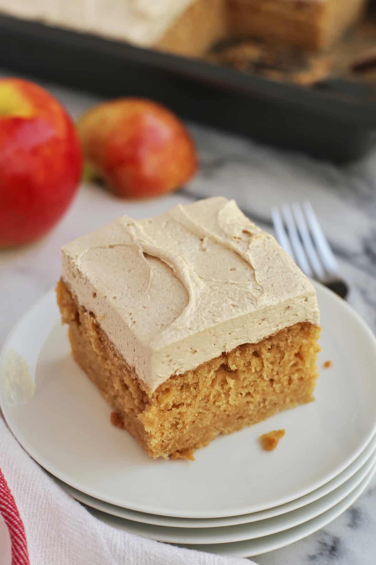 A slice of frosted apple cake on a plate with fork